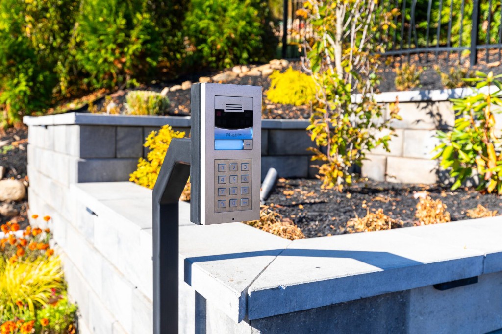 A stainless steel video intercom and keypad mounted at a garden entrance
