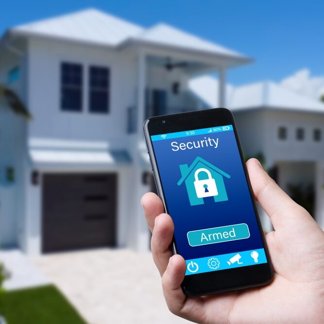 A phone showing a home security app set to armed, in front of a house