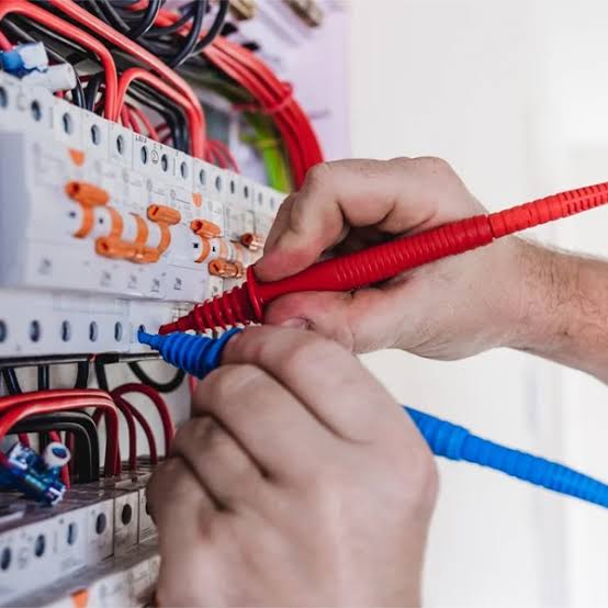 Hands testing a switchboard with red and blue meter leads